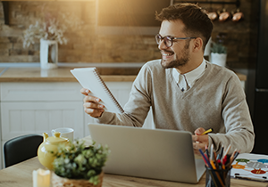 Hombre sentado frente a un portátil revisando documentos en un espacio de trabajo en casa